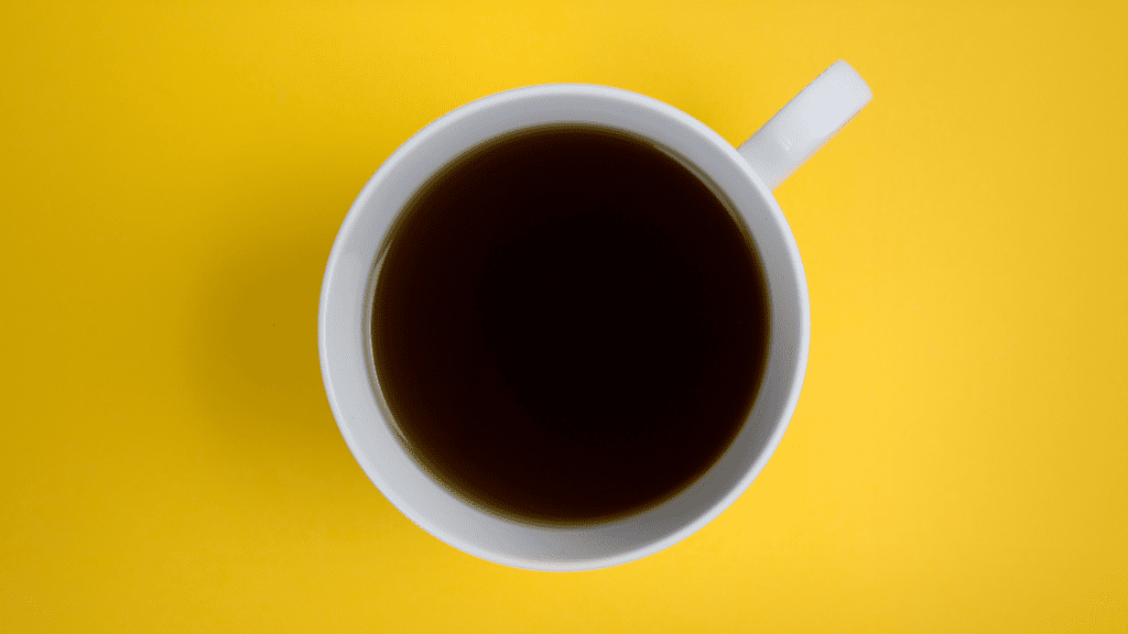 Kahvikuppi, jossa musta kahvi. Tausta keltainen.