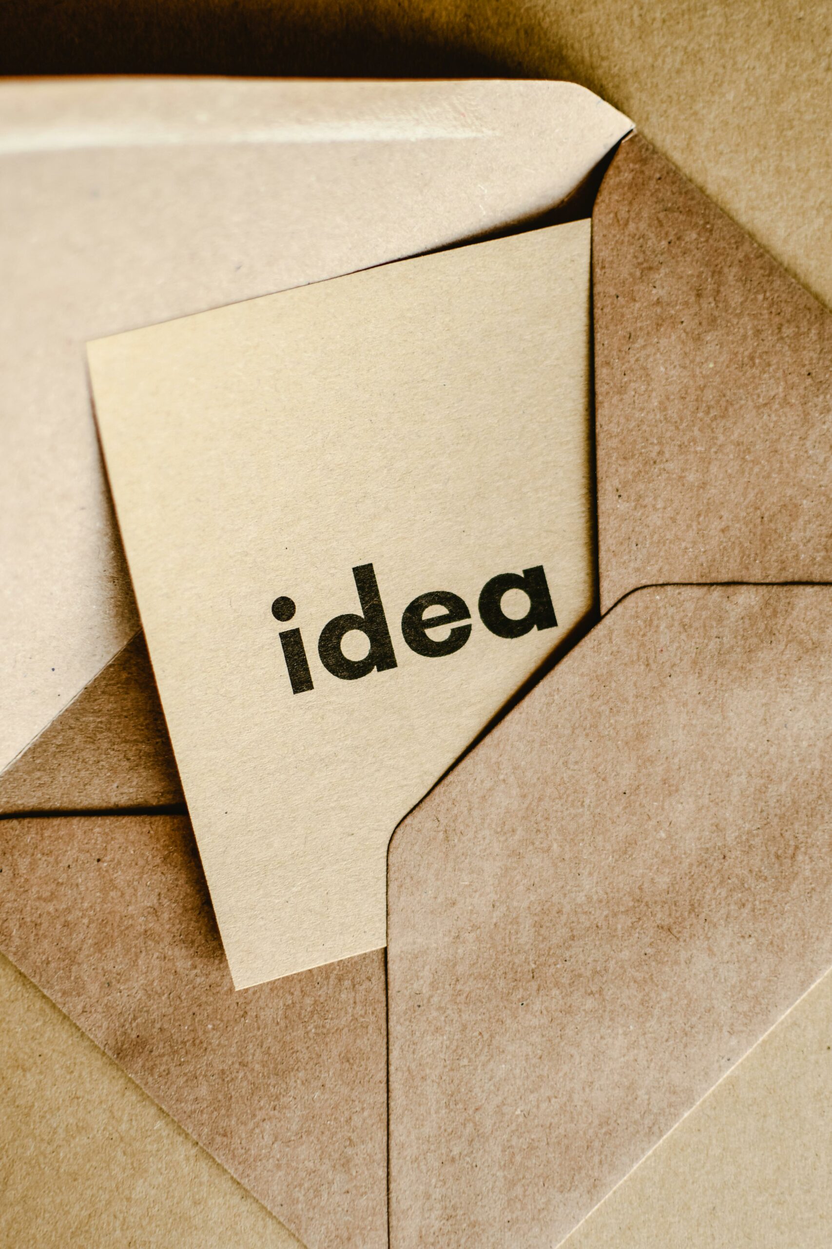ruskea kirjekuori, josta pilkistää vaaleanruskean värinen lappu, jossa lukee sana: idea