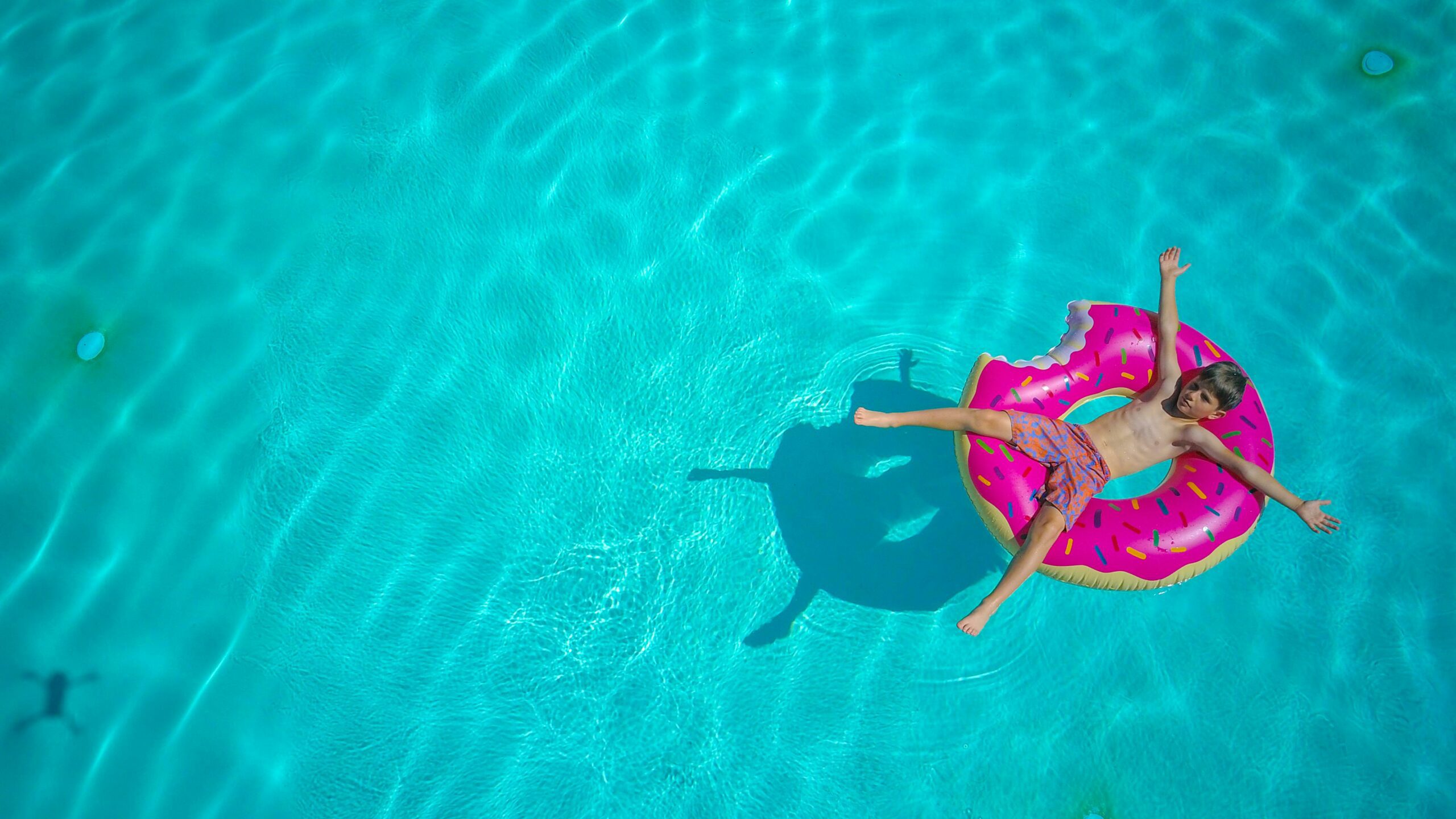 poika makaa uimahousuissa sinisessä vedessä vaaleanpunaisen uimarenkaan päällä kädet ja jalat levällä