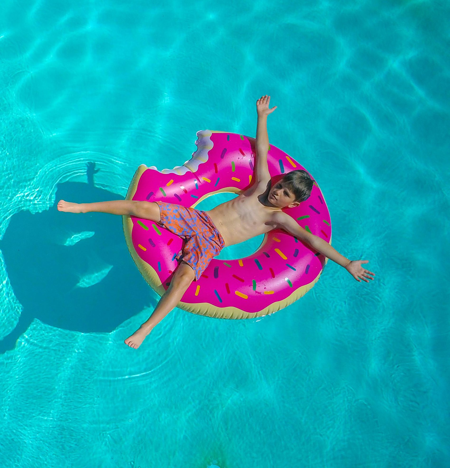 poika makaa uimahousuissa sinisessä vedessä vaaleanpunaisen uimarenkaan päällä kädet ja jalat levällä