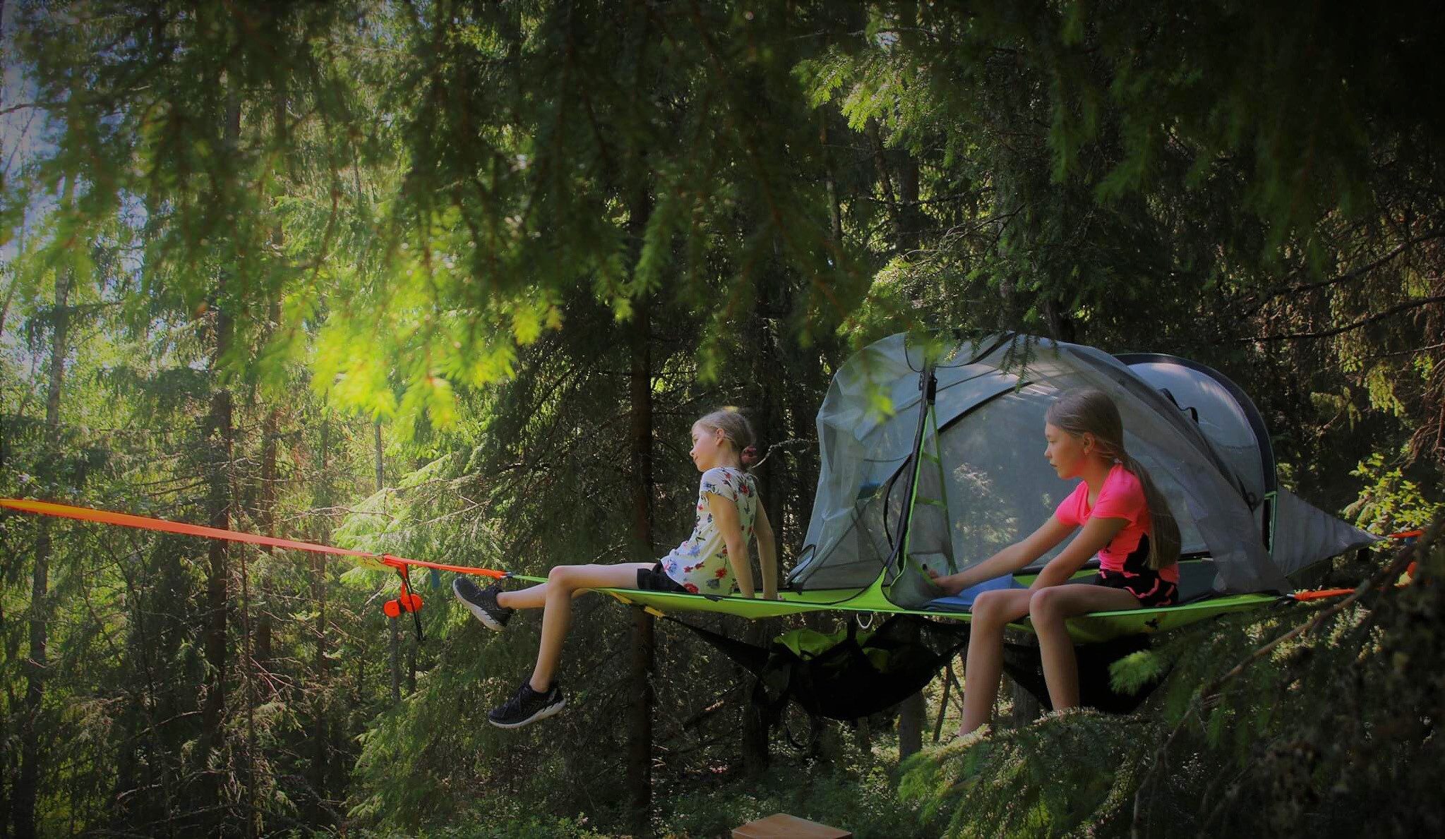 telttamajoitus puiden välissä metsässä. kaksi lasta istuu teltassa.
