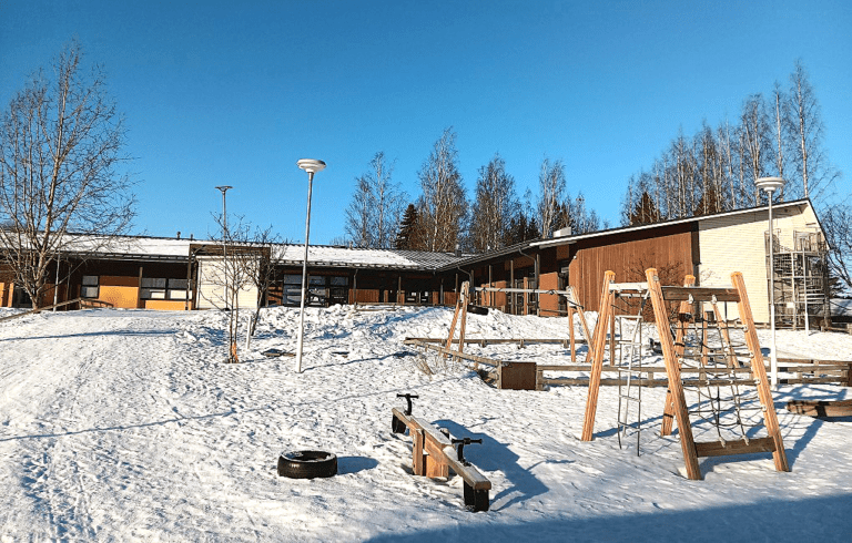 Sateenkaaren päiväkotirakennus ulkopäin kuvattuna. Pihalla lunta, sininen taivas, ruskeasävyinen rakennus.